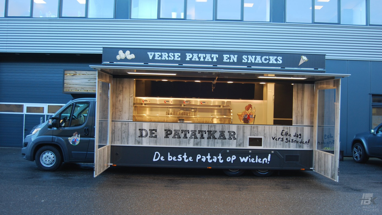 Zijaanzicht van een verkoopwagen voor patat met geopende luifel en zijborden