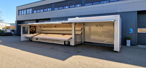 Zijaanzicht van een aanhangwagen voor groente en fruit met geopende luifel en zijbord