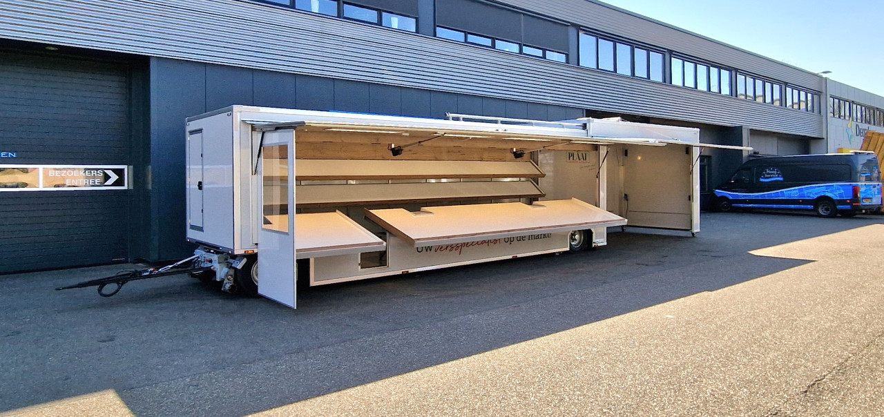 Zijaanzicht van een aanhangwagen voor groente en fruit met geopende luifel en zijbord