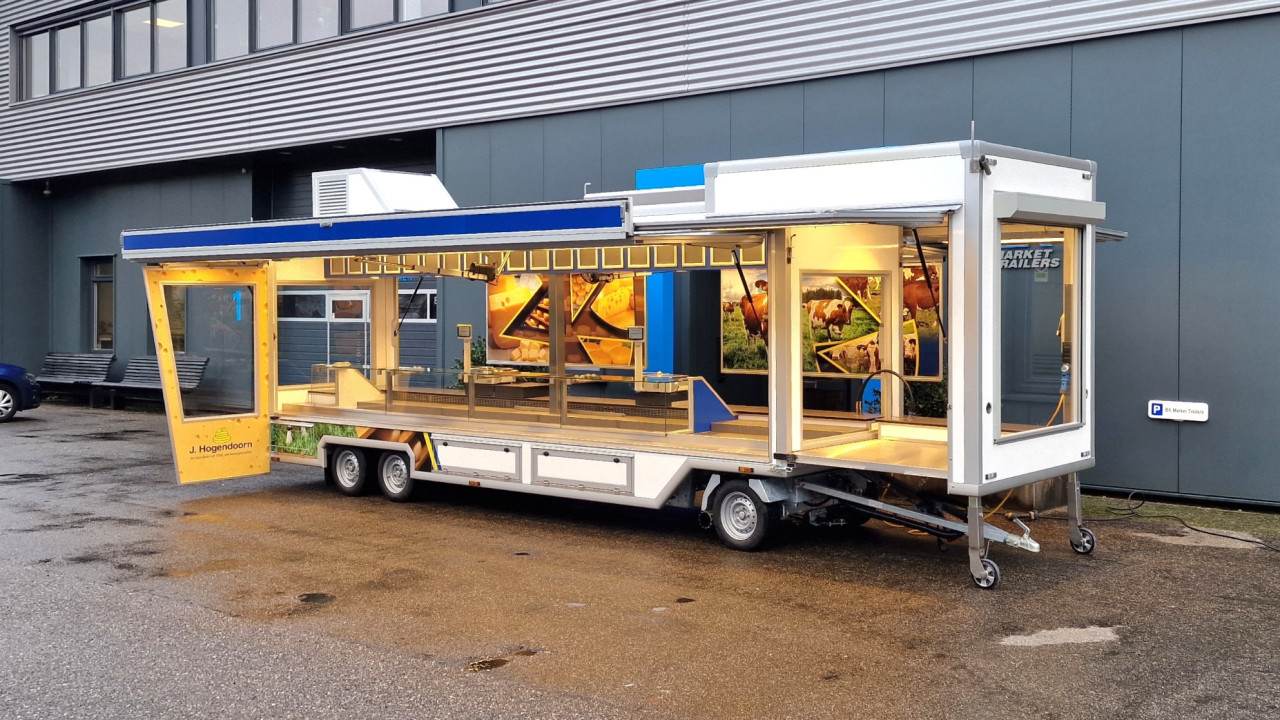 Zijaanzicht van een smalle aanhangwagen voor kaas met geopende luifel en zijbord