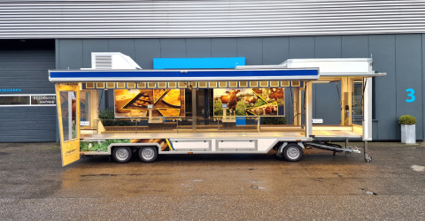 Zijaanzicht van een smalle aanhangwagen voor kaas met geopende luifel en zijbord