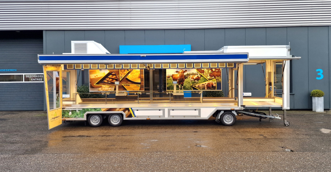 Zijaanzicht van een smalle aanhangwagen voor kaas met geopende luifel en zijbord